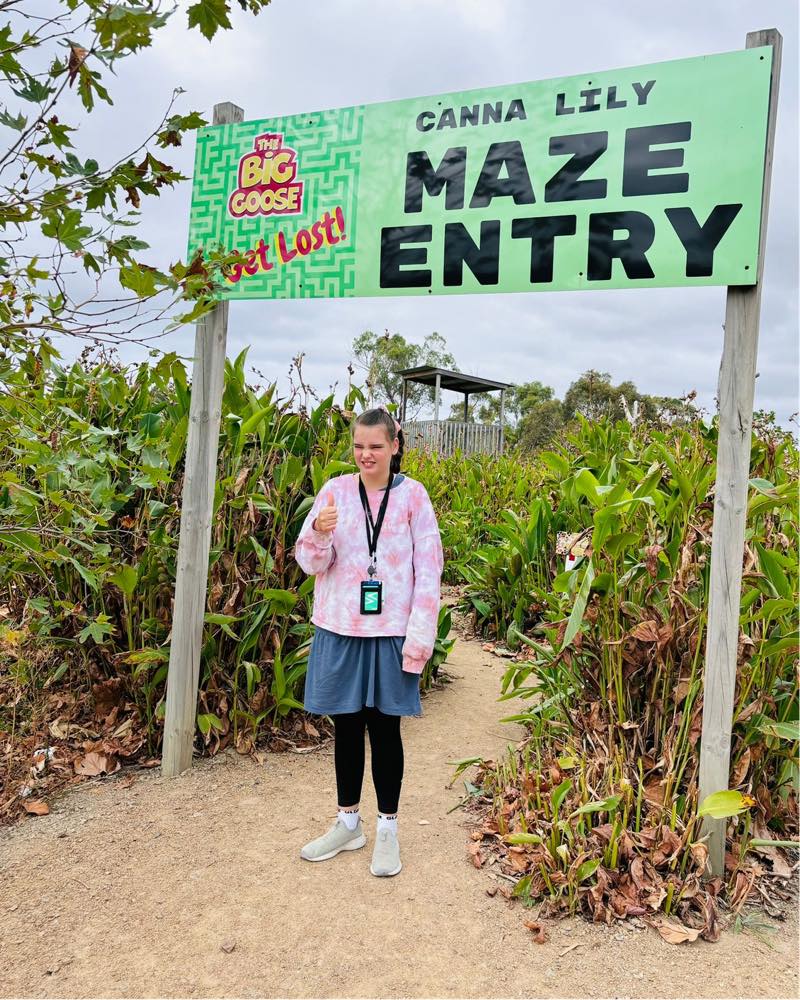 A participant at the entry to a garden maze, holding an ice cream.